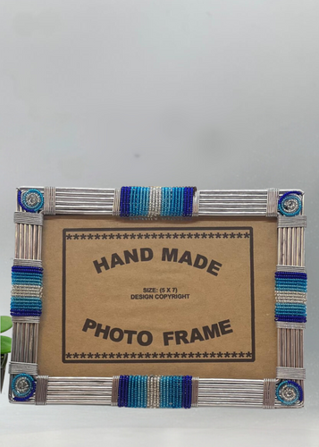 The Picha Handmade Beaded Photo Frame by Her Best Foot Forward features blue and silver beads on metal rods, handcrafted by East African women—sustainable home decor that fits a 5 x 7 photo.