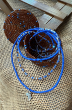 Load image into Gallery viewer, Blue beaded necklace with a brown beaded container on a textured surface
