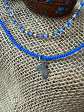 Load image into Gallery viewer, Blue beaded necklace with a silver charm of Africa on a textured surface