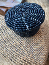 Load image into Gallery viewer, Black coil of beaded basket on a textured surface