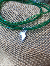Load image into Gallery viewer, Green beaded bracelet with a small silver charm of Africa on a textured fabric background