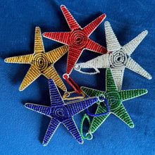 Load image into Gallery viewer, Five colorful beaded star ornaments from Her Best Foot Forward’s Reach for the Stars tax-deductible honor gift lay on blue fabric—handcrafted by East African women, supporting girls’ education with each meaningful donation.