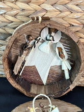 Load image into Gallery viewer, The Handmade Miniature Nativity Set by Her Best Foot Forward features Mary, Joseph, and baby Jesus crafted from natural materials in Tanzania. This fair wage Christmas decor comes in a round wooden container with a woven mat background.