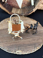 Load image into Gallery viewer, The Handmade Miniature Nativity Set by Her Best Foot Forward features a cradle with a doll and a dog, woven from natural fibers on a round wooden base—a unique fair wage Christmas decor from Tanzania.